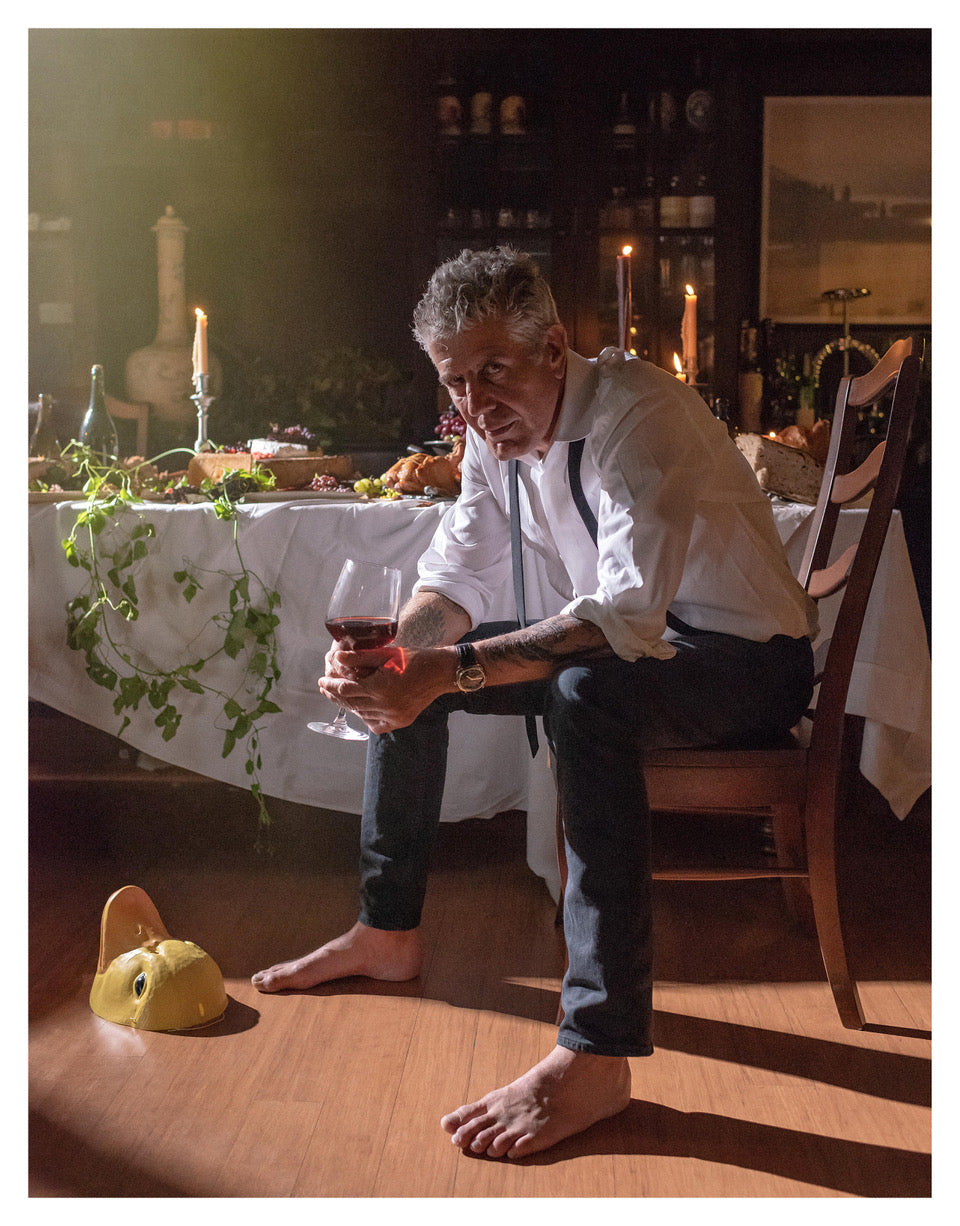 Anthony Bourdain seated with a glass of wine at a beautifully set table in his dining room